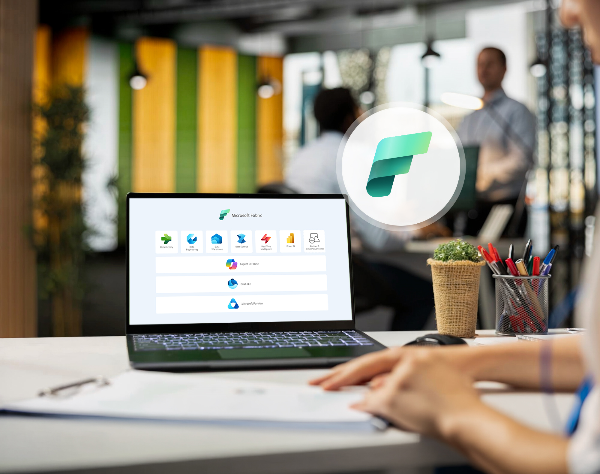 Laptop displaying Microsoft Fabric services in a modern office, with the platform logo and a team of employees in the background.